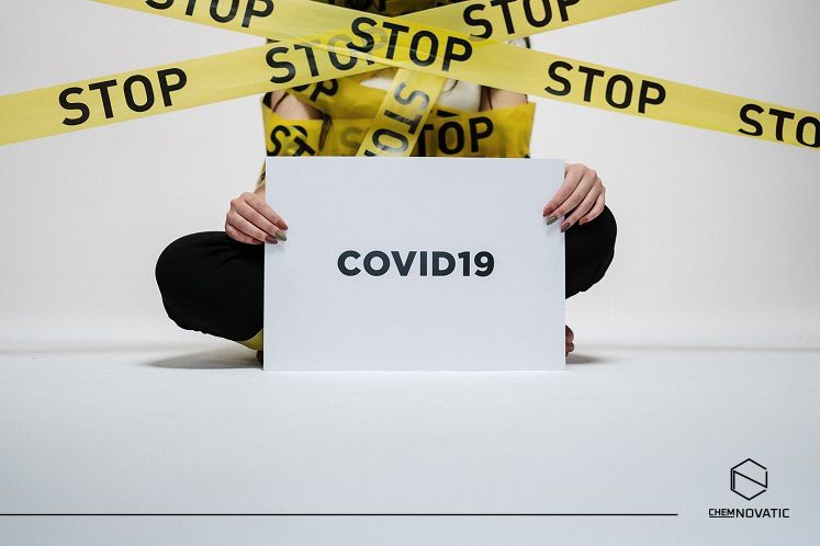 a person sitting with a card with a text: covid-19 surrounded with a tape with a text: stop