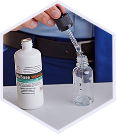 a bottle of nicbase nicotine base and a hand holding a pippete above another bottle standing near nicbase